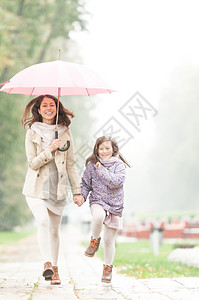 快乐的母女在公园散步漂亮的女人打着伞笑着享受下雨的天气微笑的父母图片