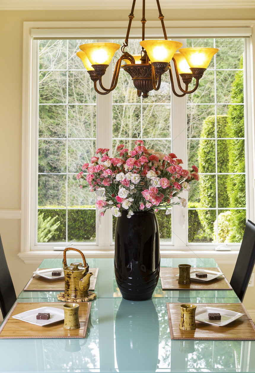 在家庭正式餐厅的竹餐垫上放着鲜花茶壶茶杯白盘和饼干的餐桌垂直照片图片