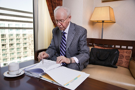 一位穿着西装打领带的老年商人坐在酒店商务休息室里图片