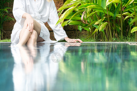 白浴袍中的浅色妇女坐在酒店的游泳池上图片