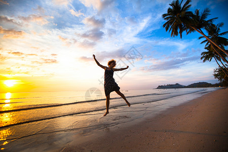 日落时在海滩上跳跃的年轻女孩图片
