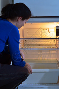 饥饿的贫穷妇女在家里空冰箱里寻找食物图片