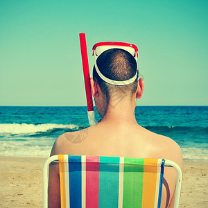 照片来自身戴潜水面具和在沙滩坐在甲板椅上滑水的男子背部图片