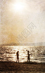 日落时在沙滩上玩耍的两个孩子剪影图片