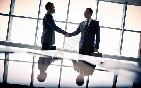 站在窗边握手的两个商人的剪影图片