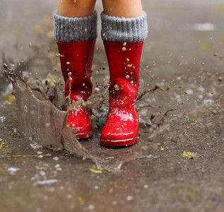 穿红色雨靴的孩子跳进水坑特写图片