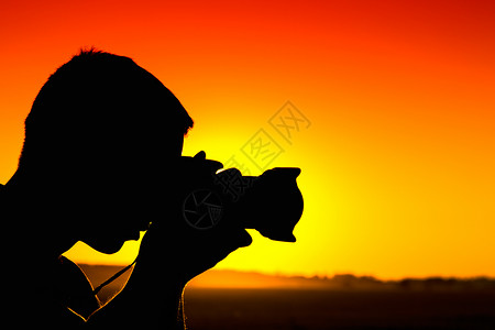日落时摄影师手持带镜头的相机的剪影图片