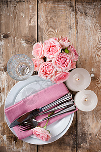 旧木板上装有粉红玫瑰蜡烛和餐具图片
