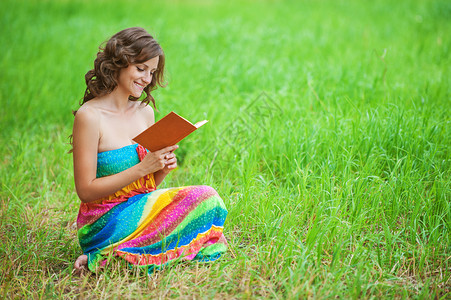身穿橙色毛衣在夏日绿色公园持有书籍的年轻漂亮的黑头发卷图片