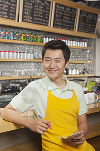 笑的年轻咖啡师的肖像用一张垫子和笔背景图片