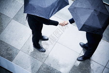 两名持雨伞和握手的商人的高角度视野背景图片