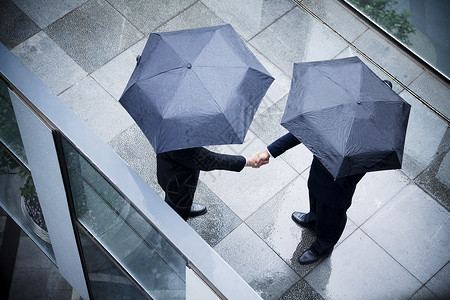 两名持雨伞和握手的商人的高角度视野背景图片