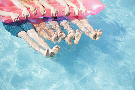 一个游泳池中四个朋友的低位朋友抱着一个可充气的木筏脚图片