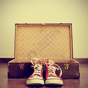 一对红色运动鞋在开着的旧棕色手提箱前图片