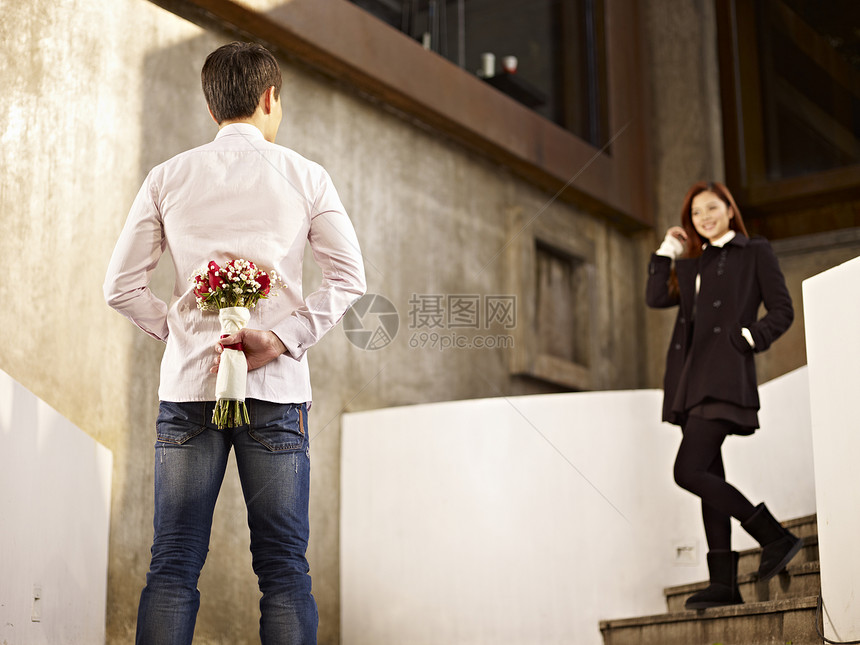 亚裔年轻男人在台阶边等女友后面拿着鲜花等图片