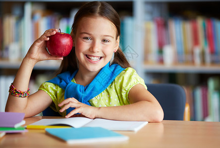 快乐女学生的肖像和大红苹果在图书馆图片