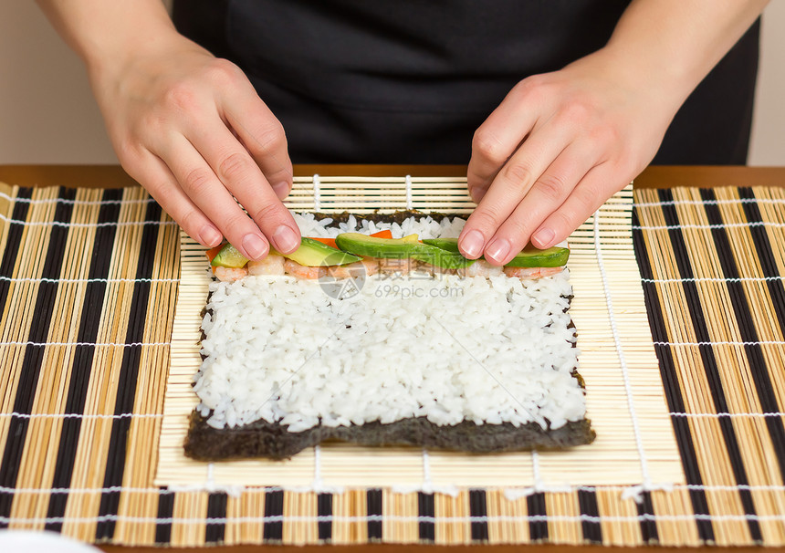 女厨师的手用米鳄梨和虾卷起日本寿司图片