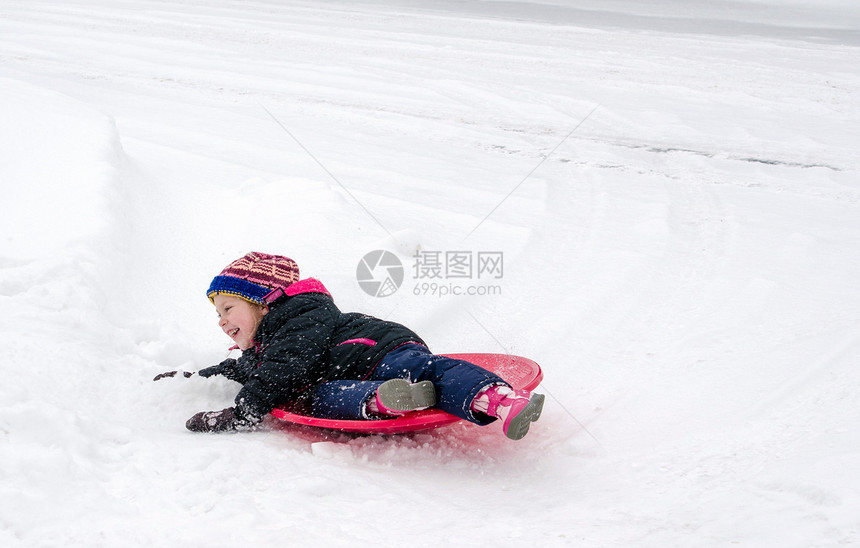 一个欢笑的女孩在雪盖山丘的底部擦干净图片