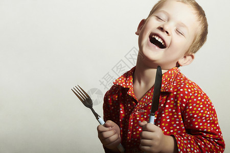 有趣的小英俊男孩用叉子和刀子的画像饥饿的孩子微笑图片