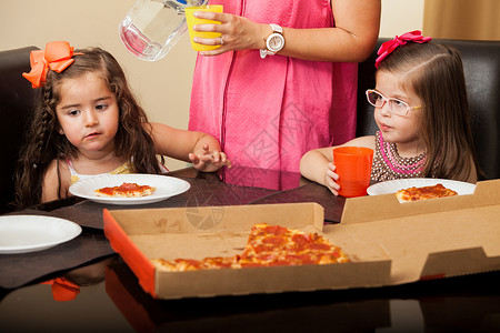 美丽的小朋友在家吃比萨饼而母亲监管图片
