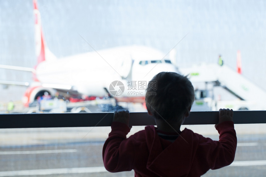 在机场看飞机的小男孩背对着镜头站在一个俯瞰停机坪的大图片