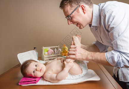 父亲在更换尿布和为背景婴儿设置的卫生设备之后图片