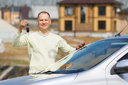 幸福的人拿着车钥匙在房子的背景上图片