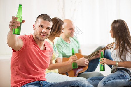 一个年轻男人在家庭聚会上微笑喝着啤酒和欢呼她的朋友图片