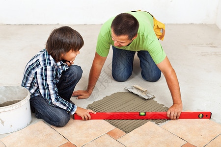 男人和男孩一起铺制陶瓷地板砖用精神水平检图片
