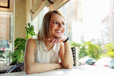 坐在咖啡馆看窗的年轻快乐女人图片