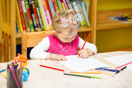 可爱的小女孩在幼儿园的桌子上用彩色铅笔画图片