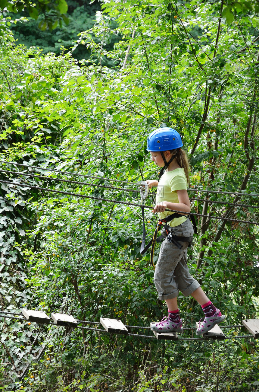 一名前童女孩在高树之间的梯子上行走图片
