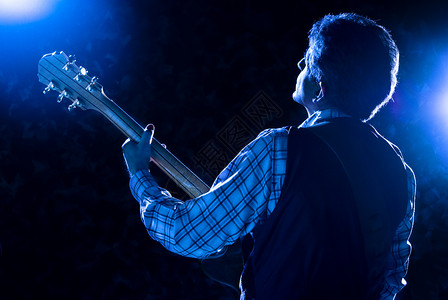 舞台上的吉他手在蓝光下弹吉他图片