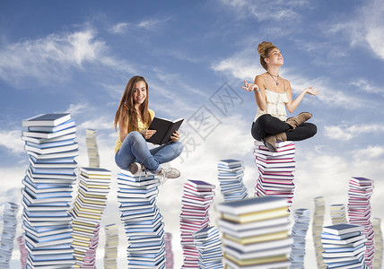 两个学生坐在高的书堆上图片