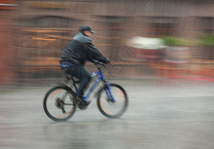 潮湿的骑自行车者在雨季乘车穿过街道故意图片