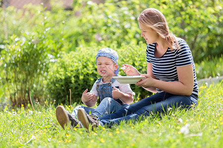 可爱的小男孩在草地上吃户外食物母亲对拉着一个漫画脸的食图片