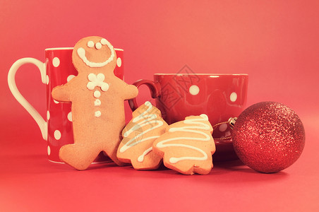姜饼人与红色圆点咖啡杯和茶杯与圣诞树形状饼干红色背景复图片