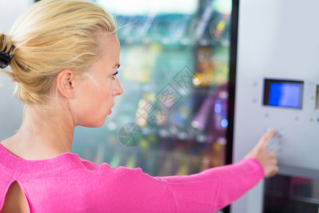 白种女人用自动售货机送零食她正在看机器的蓝色显示屏图片