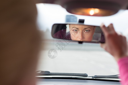 美丽的年轻女士从车前座的后视镜中回望过来背景图片