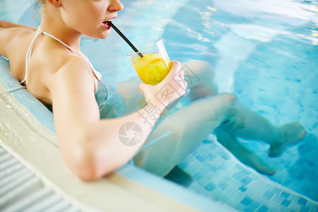 年轻女子坐在泳池边喝柠檬水图片