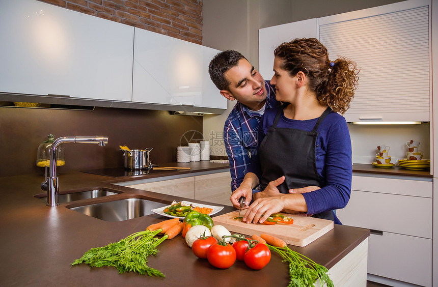 热恋中的情侣在厨房里拥抱和准备健康的蔬菜现代家庭图片