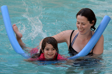 年轻母亲教孩子女孩年龄为04岁在游泳池里游泳图片