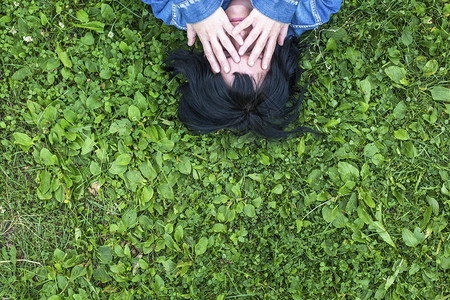 躺在草地上的年轻女人用双手蒙住她的脸图片