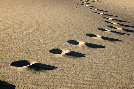 夕阳在谷的沙丘上突出了一组孤独的脚印图片