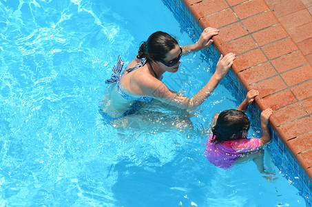 年轻母亲教孩子在游泳池游泳然后图片