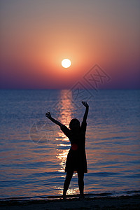 女孩日落时在海面上伸展浅图片