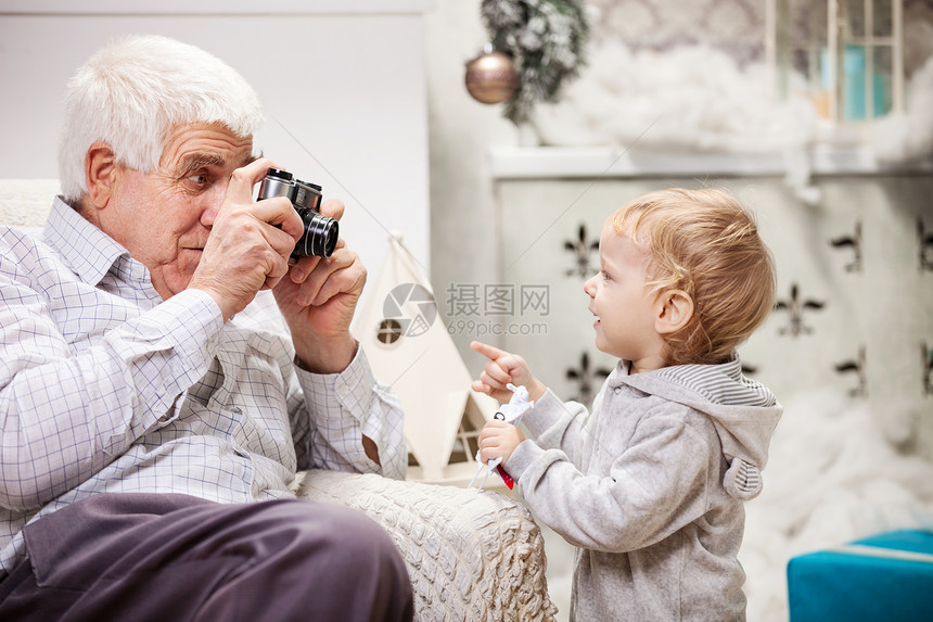 老人在圣诞节给他蹒跚学步的孙子拍照图片