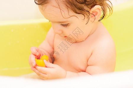 小孩子坐在绿色浴缸里咀嚼玩具图片