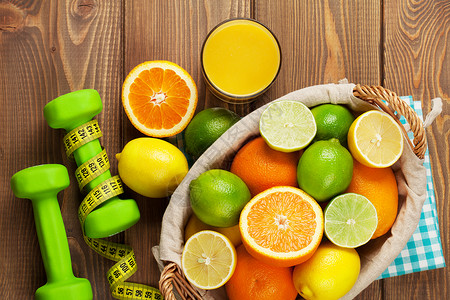 篮子和哑铃中的柑橘类水果橙子酸橙和柠檬在木桌背景上图片