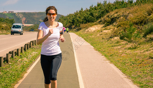 运动的年轻女子戴着耳机在户外跑道上跑步时从她的智能手机听音乐现代健康图片